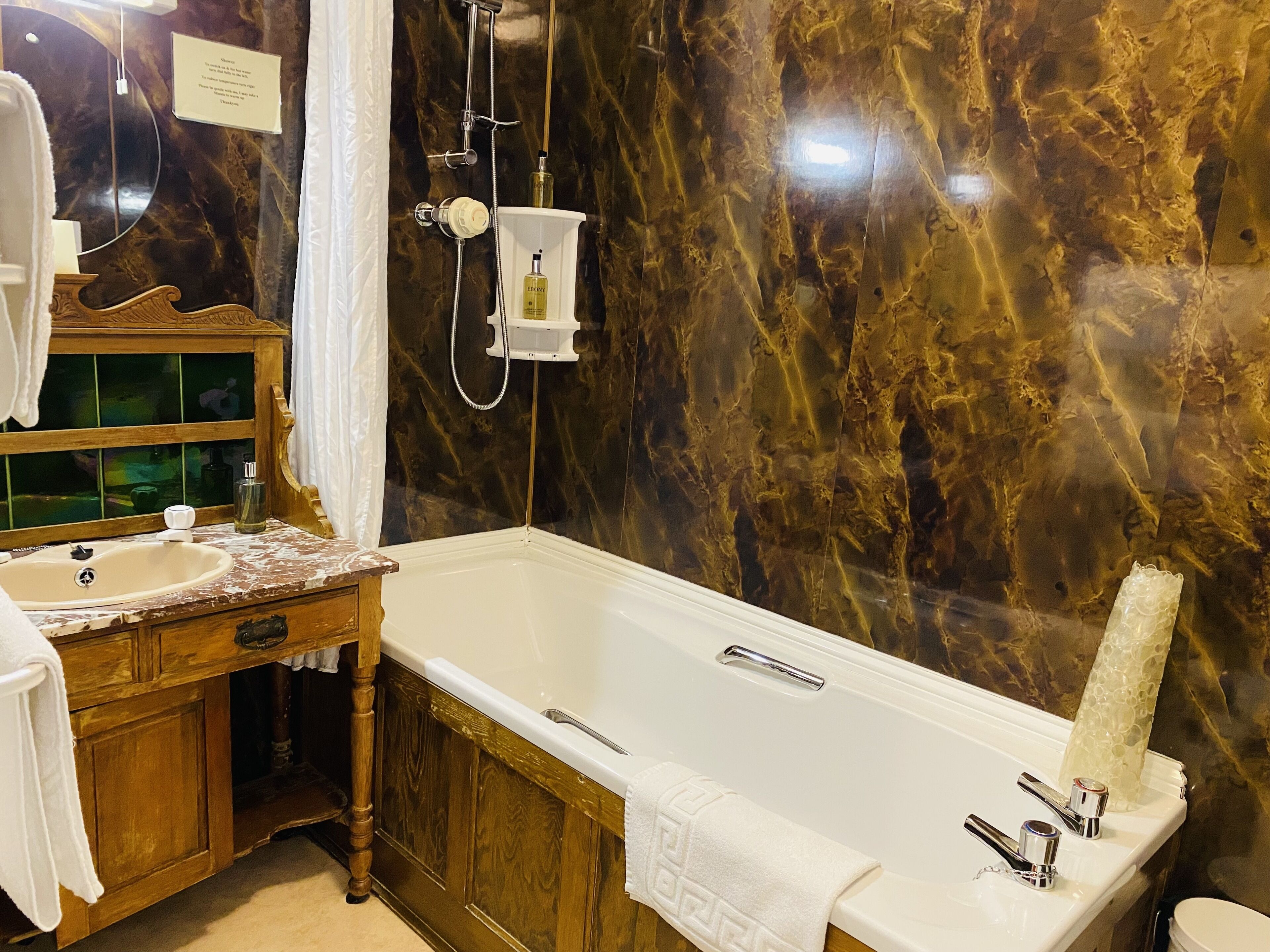 A bathroom with a marble wall, a bathtub, a wooden vanity with a mirror, and a sink.