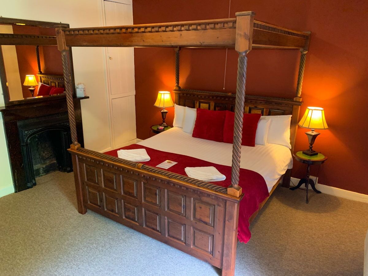 A four-poster bed with a wooden frame, white bedding, and red pillows. There are two bedside tables with lamps.