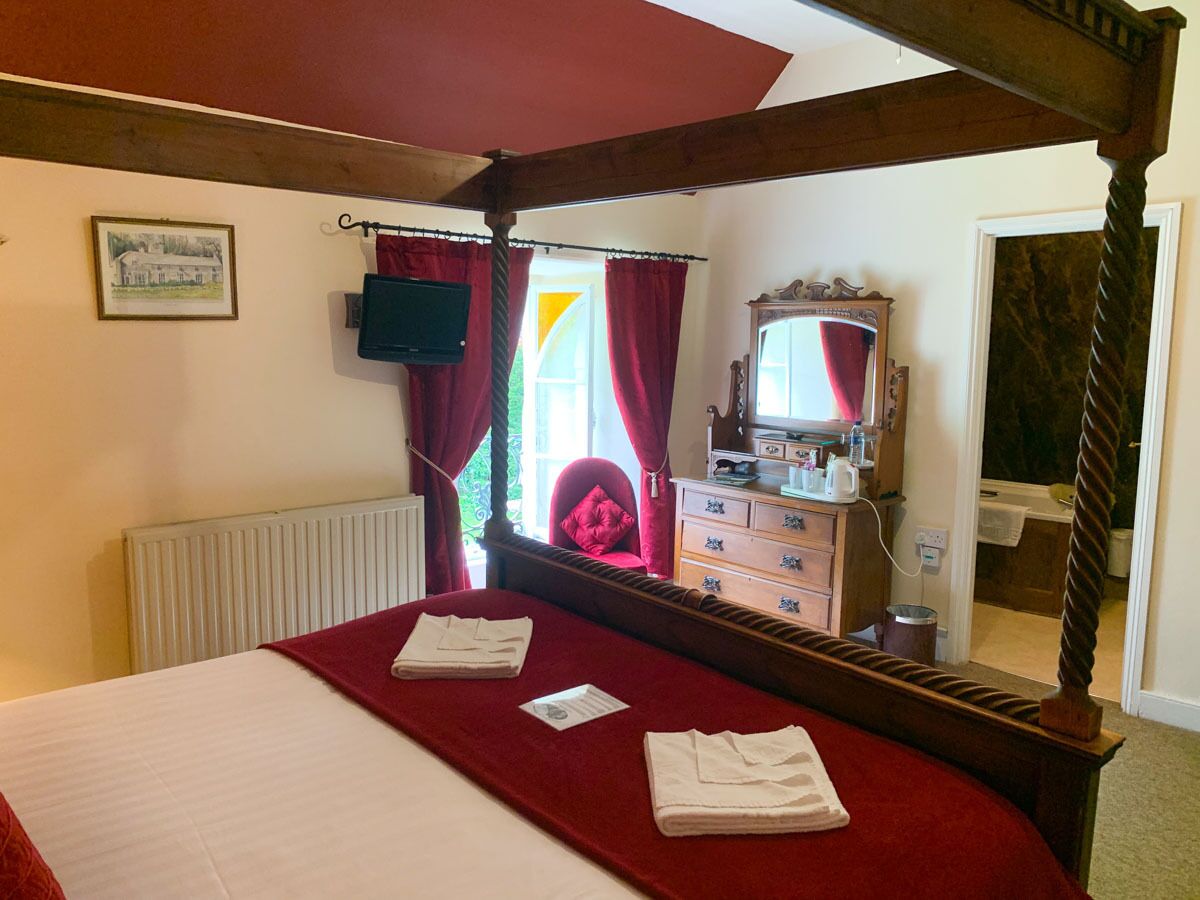 A bedroom with a four-poster bed, a dresser with a mirror, and a window with red curtains.