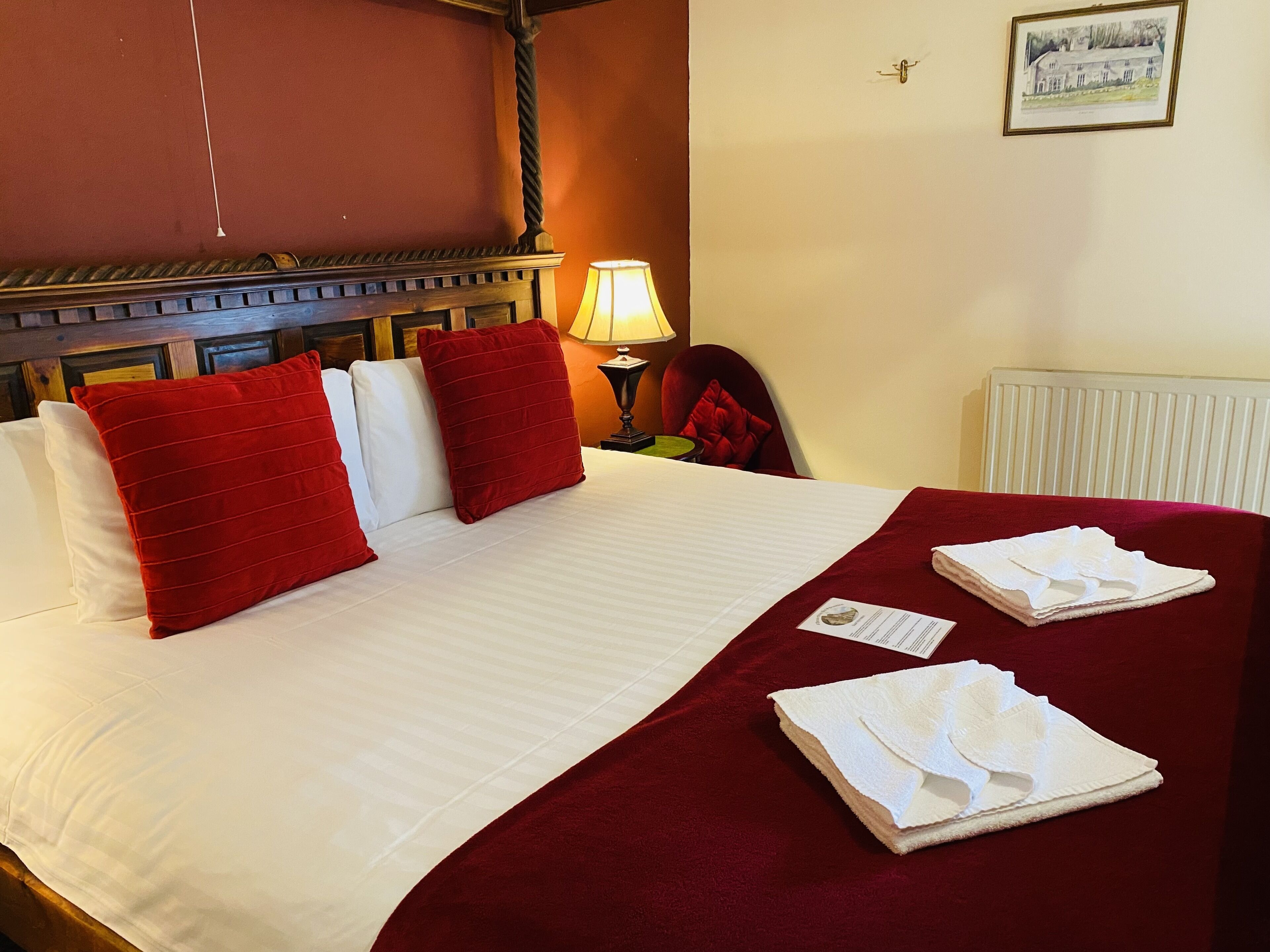 Habitació d'hotel amb un llit, almoines vermelles i blanques, una manta vermella i una tovallola doblegada al llit.