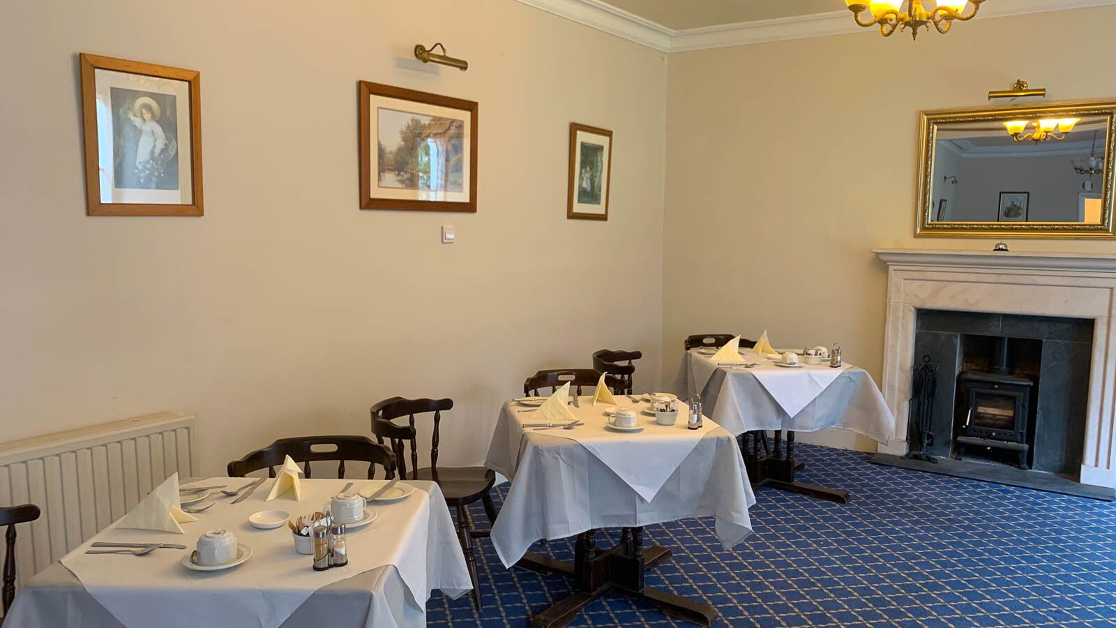 A dining area with tables set for four, a fireplace, and framed pictures on the wall.