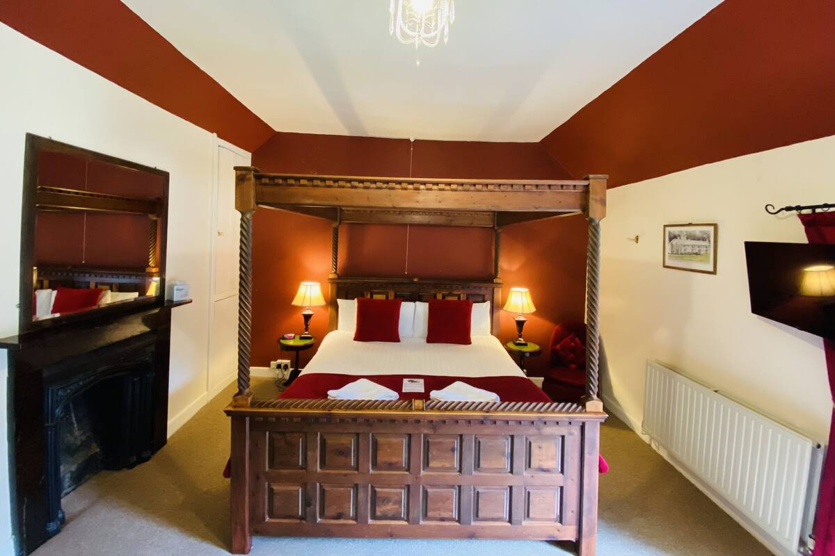 A four-poster bed with a wooden headboard, two bedside tables with lamps, a fireplace, and a radiator.