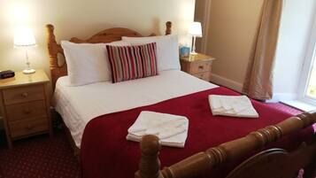 A neatly made bed with white linens and a red blanket, wooden headboard, bedside tables with lamps, and a window with curtains.