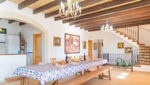 A dining area with a long table set for a meal, wooden benches, a chandelier, and a staircase in the background. - SON PUJOL - Villa with private pool in MONTUÏRI. Free WiFi (Montuïri)