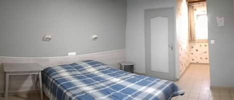 A bedroom with a bed, a desk, and a door leading to another room.