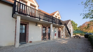 A building with a gravel driveway, a covered outdoor seating area, and a staircase leading to a balcony. - Auberge du Tranchoir (Nevoy)