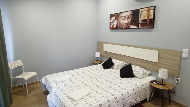 A bedroom with a bed, a chair, a red rug, and a wall-mounted air conditioner. - Good Vibes - Lagos Guest House (Lagos)