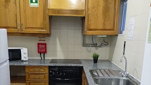 A kitchen with wooden cabinets, a microwave, a dishwasher, a sink, and a fire extinguisher. - Good Vibes - Lagos Guest House (Lagos)