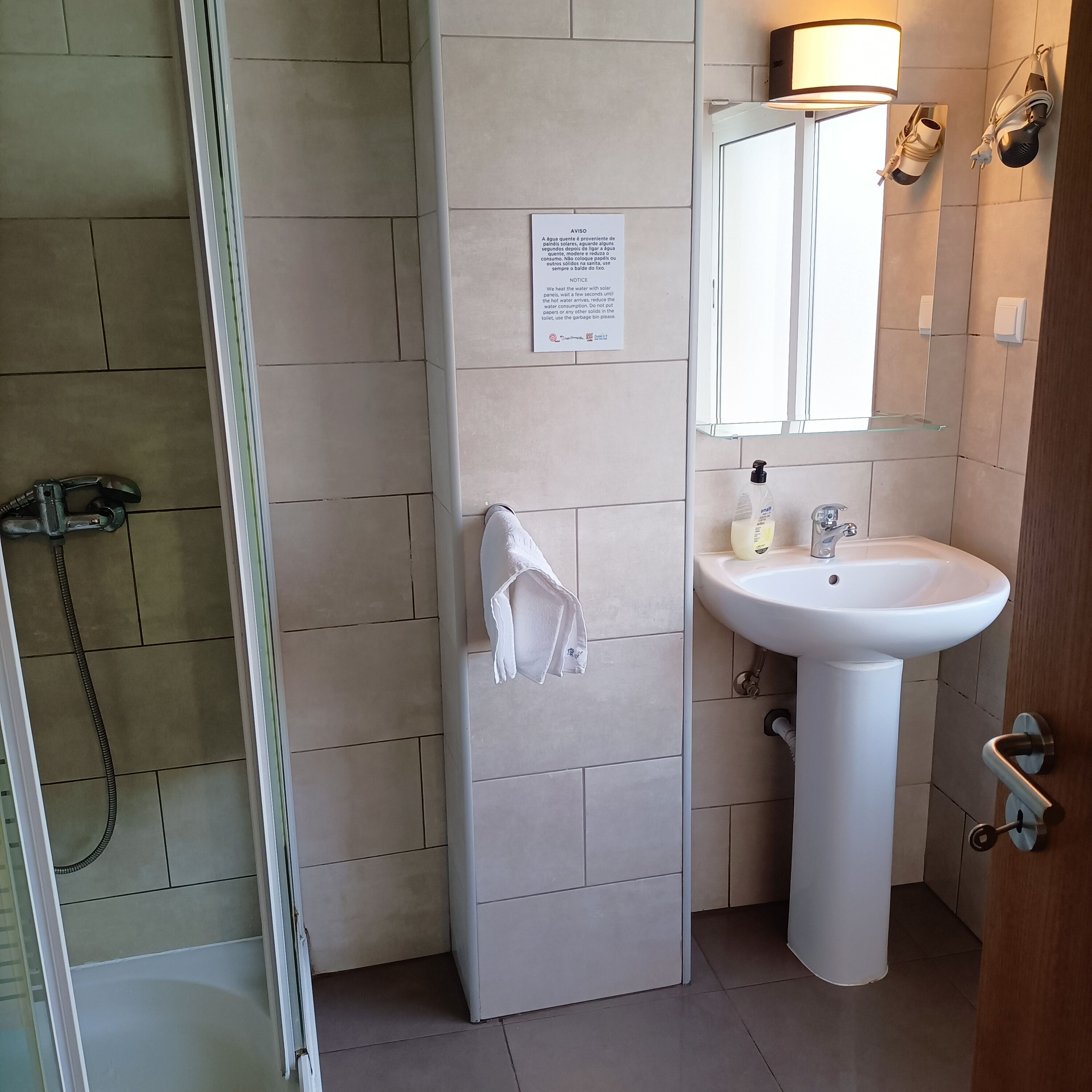 Un baño con ducha, lavamanos y espejo. Hay una toalla colgada en la pared y un cartel con instrucciones.