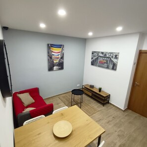 A modern living room with a red sofa, a wooden dining table, and a small black chair. There is a wooden bench against the wall and a framed picture above it. - Good Vibes - Lagos Guest House (Lagos)