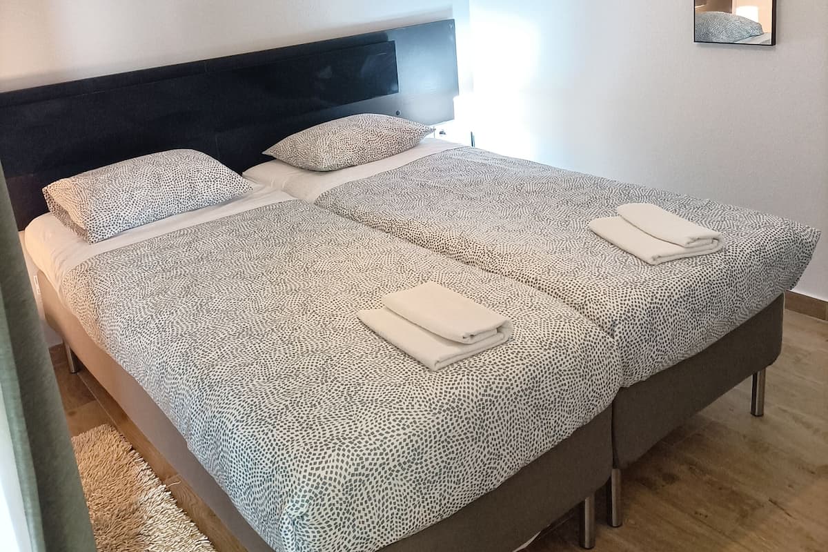 A neatly made bed with patterned bedding, a headboard, and a wall-mounted mirror.