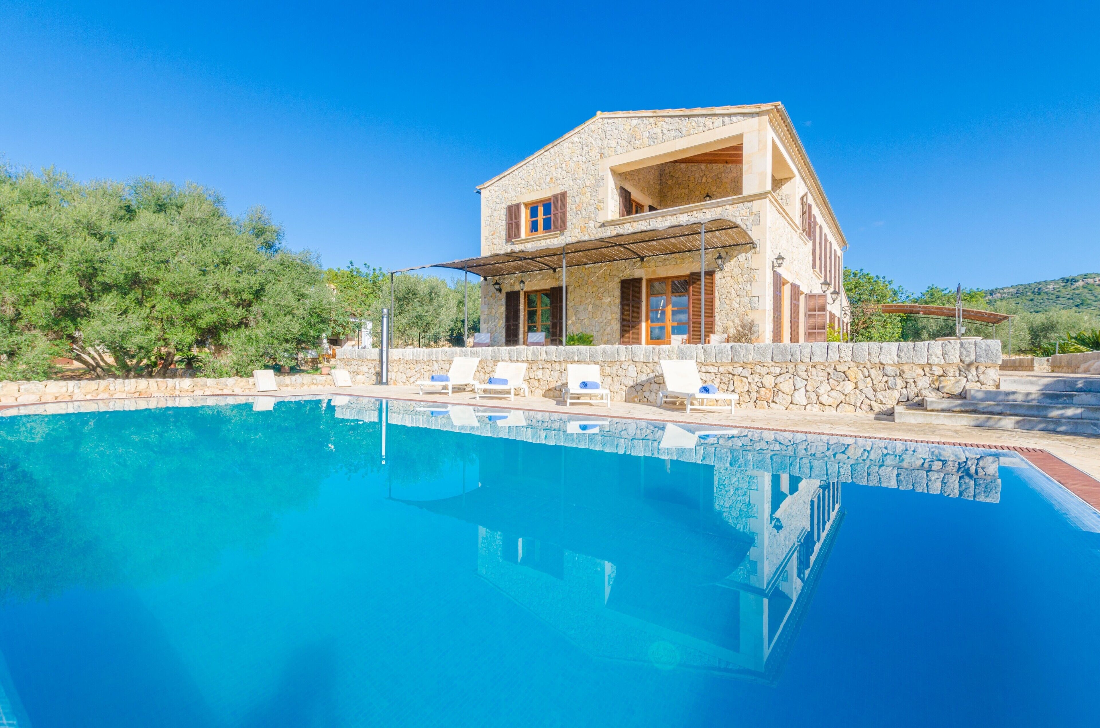 A stone house with a swimming pool, outdoor lounge chairs, and a clear blue sky.