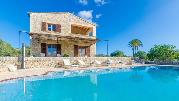 Ein zweistöckiges Steinhaus mit Schwimmbad, Liegestühlen und einer überdachten Terrasse.