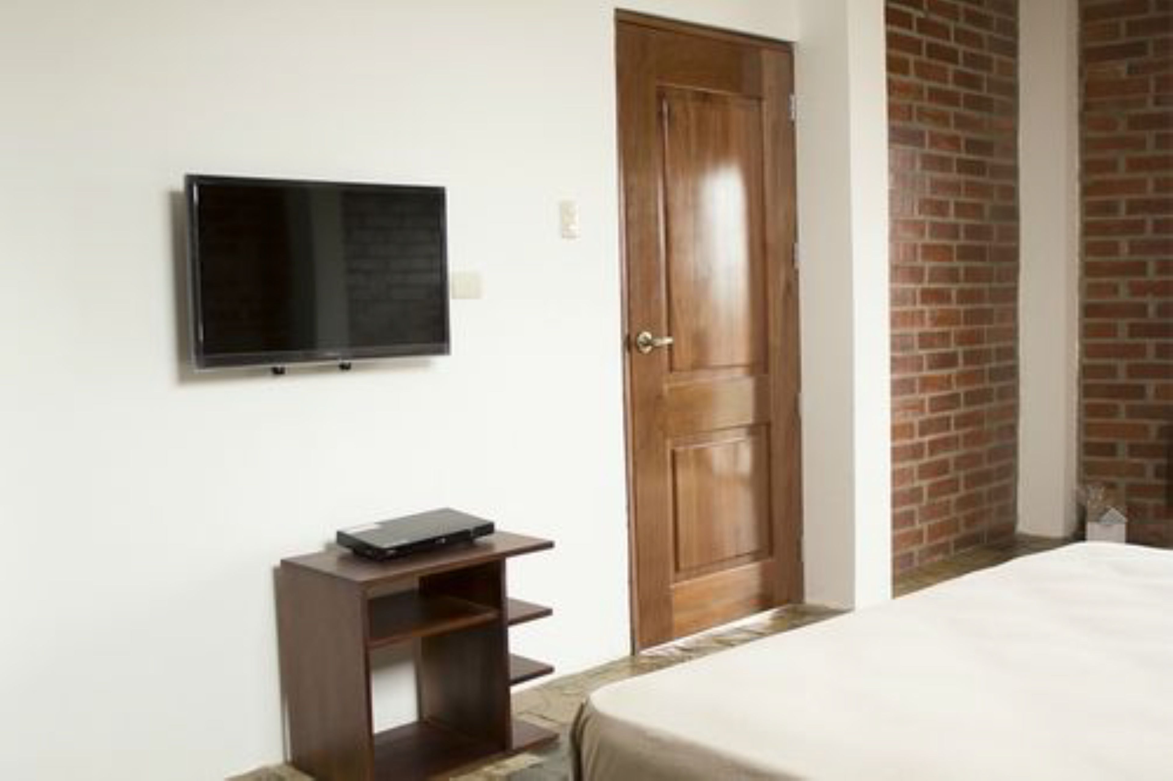A hotel room with a bed, a TV mounted on the wall, a wooden door, and a brick wall.