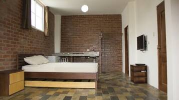 Una habitación con una cama, una mesita, un televisor y una pared de ladrillo.