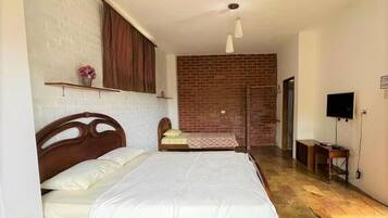 Un dormitorio con dos camas, una pared de ladrillo, un televisor y piso de madera.