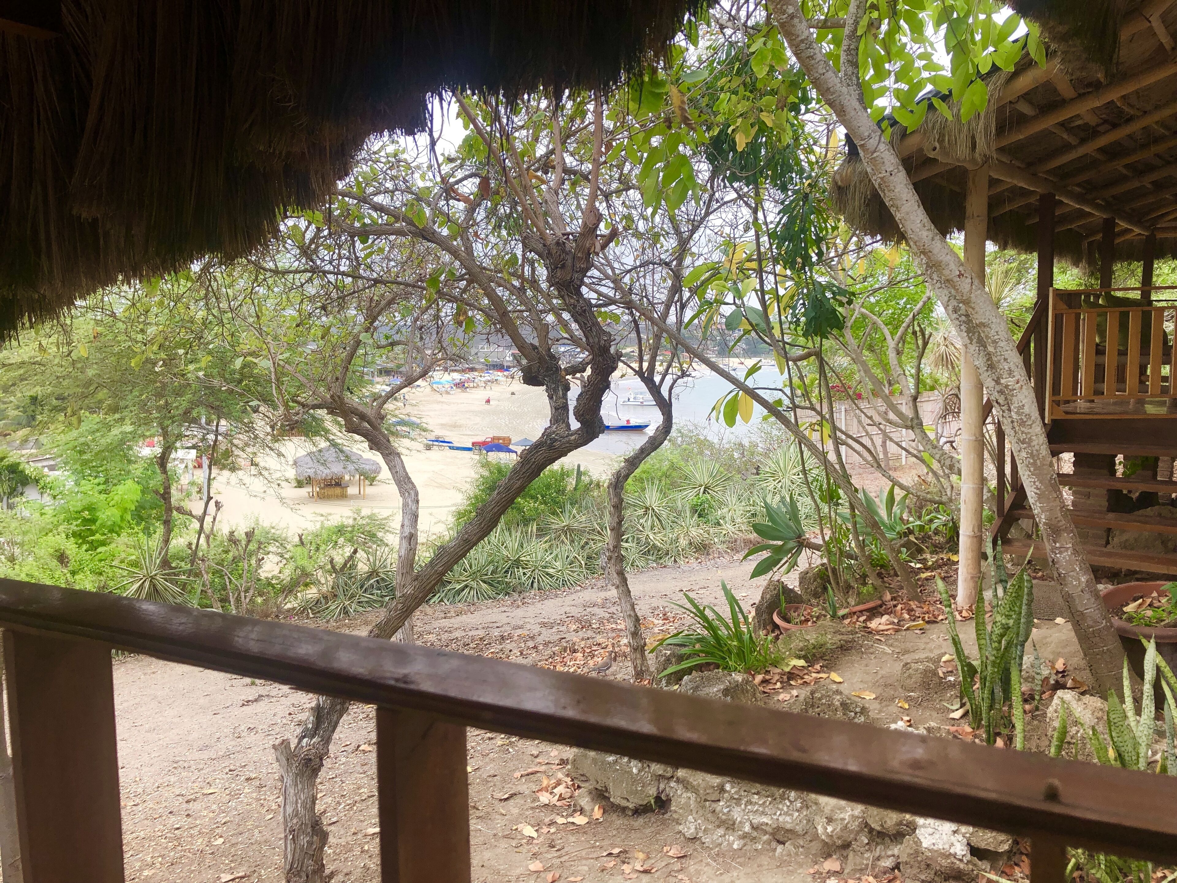 A wooden deck with a view of a beach area, including a boat and beach umbrellas.