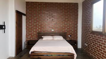 Un dormitorio con pared de ladrillo, estructura de cama de madera, mesita de noche y ventana.