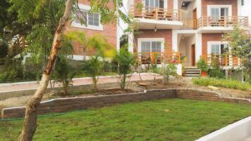 Un edificio de dos pisos con fachada de ladrillo, un balcón en el nivel superior y un pequeño jardín con césped y plantas.