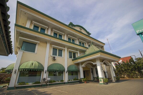 A multi-story hotel with a green and white facade, large arched windows, and a prominent entrance with columns. - RedDoorz Plus near Alun Alun Kejaksan Cirebon (North Cirebon)