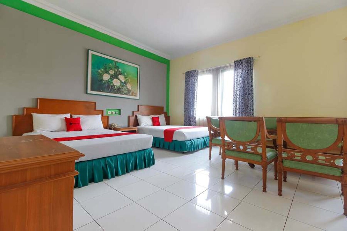 A hotel room with two beds, a wooden desk, a chair, a painting on the wall, and a window with curtains.