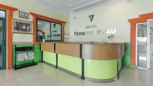 A hotel reception area with a green and orange color scheme, a reception desk, framed pictures on the wall, and a sign that reads "HOTEL PERNIATA HI AU". - RedDoorz Plus near Alun Alun Kejaksan Cirebon (North Cirebon)