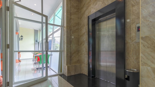 An interior with a glass door leading to a seating area, a marble wall, and an elevator. - RedDoorz Plus near Alun Alun Kejaksan Cirebon (North Cirebon)