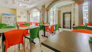 A dining area with tables and chairs, large windows, and a clock on the wall. - RedDoorz Plus near Alun Alun Kejaksan Cirebon (North Cirebon)