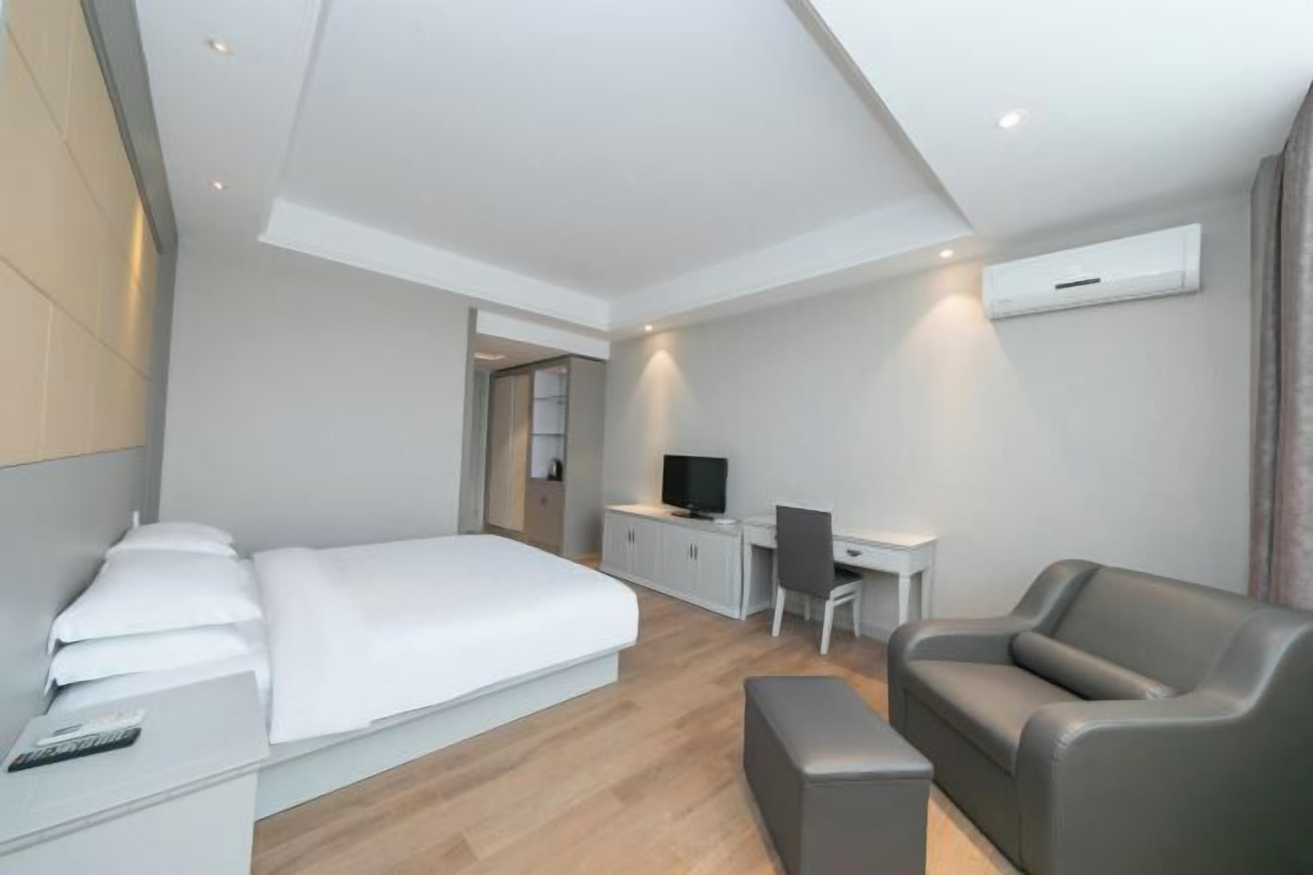 A modern hotel room with a bed, a desk, a chair, and a sofa.