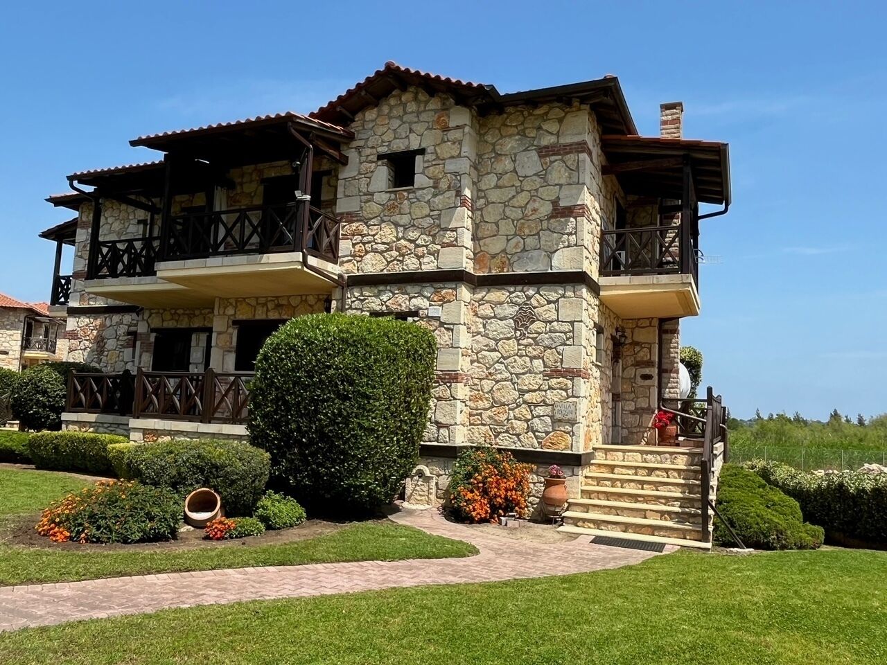 Un bâtiment en pierre de deux étages, doté d’un balcon, d’un escalier en pierre et d’un jardin bien entretenu.