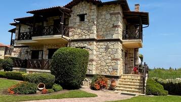 A two-story stone building with a balcony, a stone staircase, and a well-maintained garden.