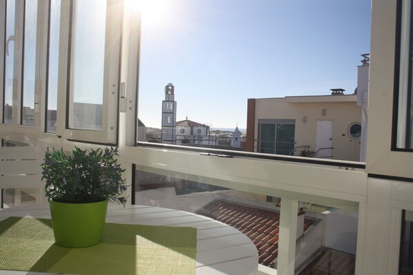 A balcony with a potted plant, a table, and a view of buildings and a tower in the distance.