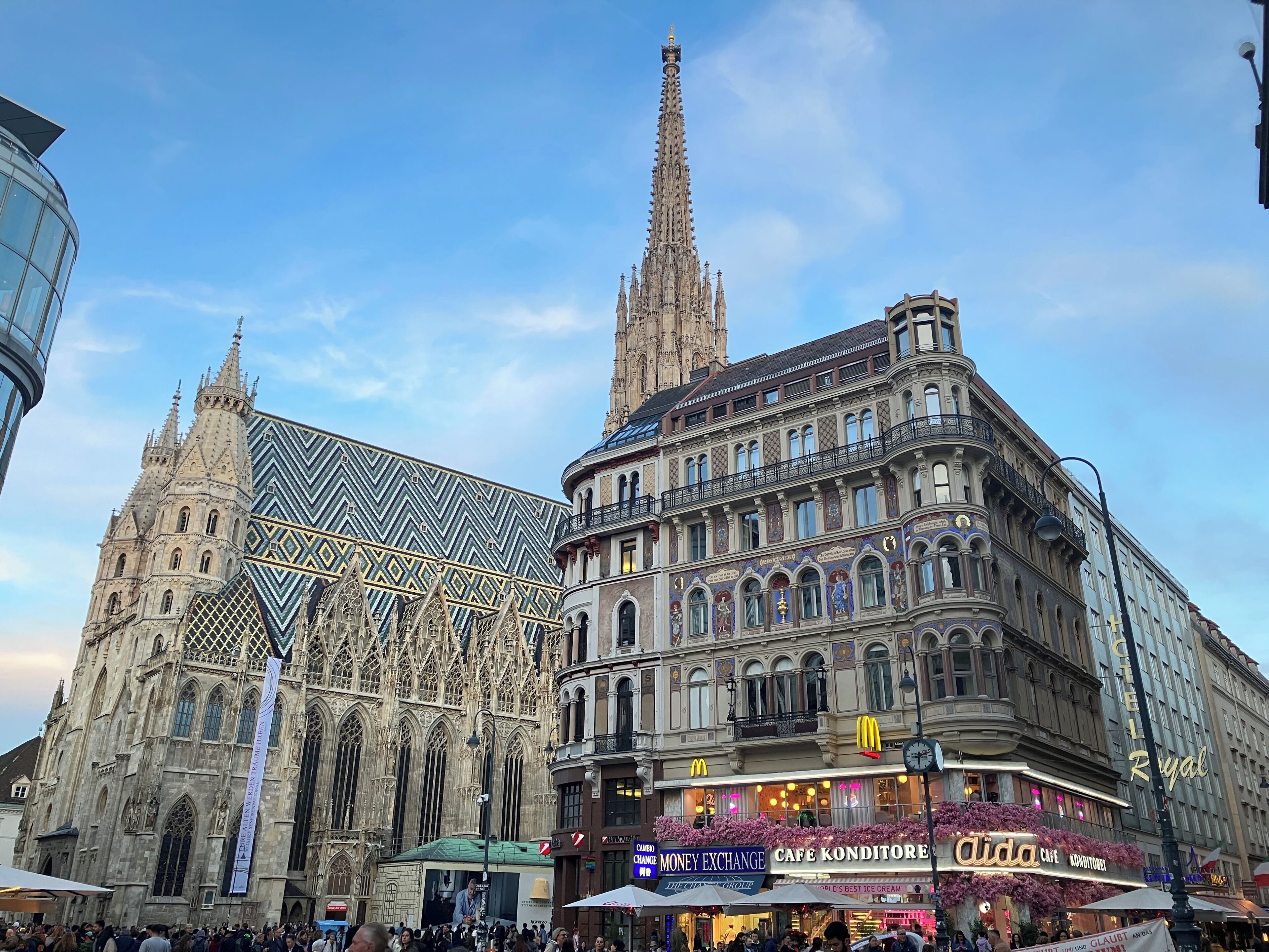 A historic cathedral with intricate Gothic architecture, a modern glass structure, and a commercial building with various shops and a prominent McDonald's sign.