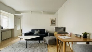 Ett modernt vardagsrum med en soffa, ett litet bord och en stol. Det finns ett element, ett fönster och en inramad tavla på väggen.