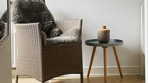 Ett rum med en flätad fåtölj, ett litet runt bord med en skål på och en inramad karta på väggen.