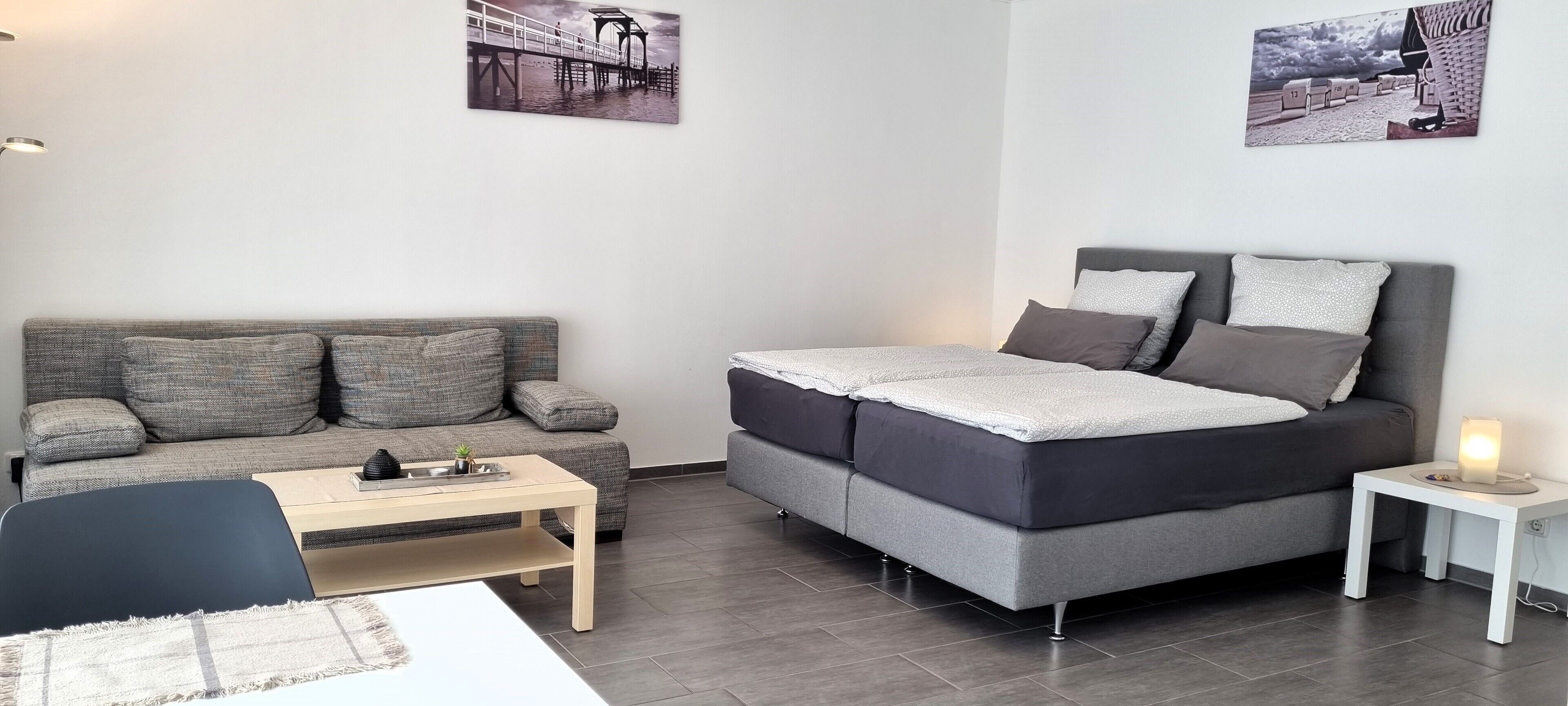 Un salon moderne avec un canapé gris, un canapé-lit gris, une petite table et une table de chevet avec une lampe.
