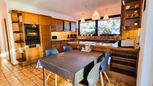 Una cocina moderna con armarios de madera, una mesa de comedor con sillas, un horno empotrado y una ventana con vistas a la vegetación.