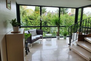 A modern living room with a large window, a sofa, a small round table, and a staircase.