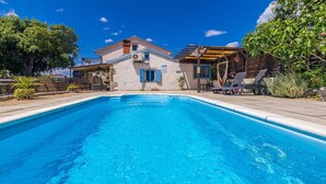 A swimming pool with a clear blue water, surrounded by a wooden deck and lounge chairs. - Rustic holiday house DEPOPE with private pool (Skrpčići)