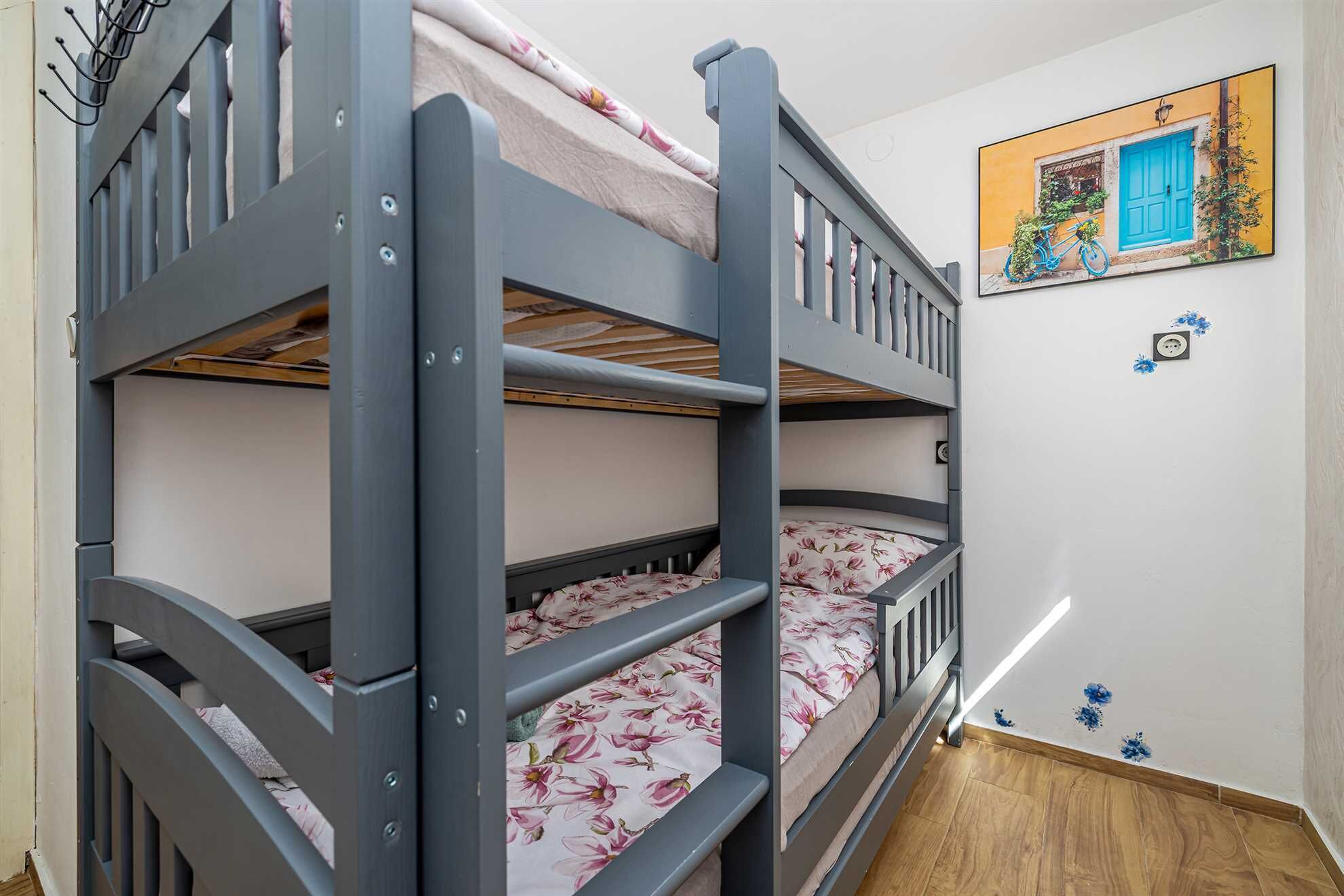 A bunk bed with floral bedding, a wall-mounted picture, and a power outlet.