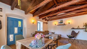 A cozy room with a wooden ceiling, a blue door, a wooden table with a vase of flowers, and a brown sofa. - Rustic holiday house DEPOPE with private pool (Skrpčići)