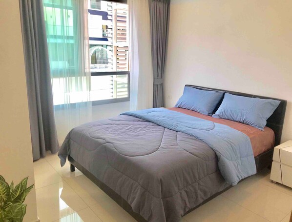 Quarto com cama, cortinas, mesa de cabeceira e um vaso com planta.
