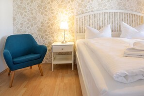 Een hotelkamer met een bed, nachtkastje, lamp en een blauwe fauteuil.