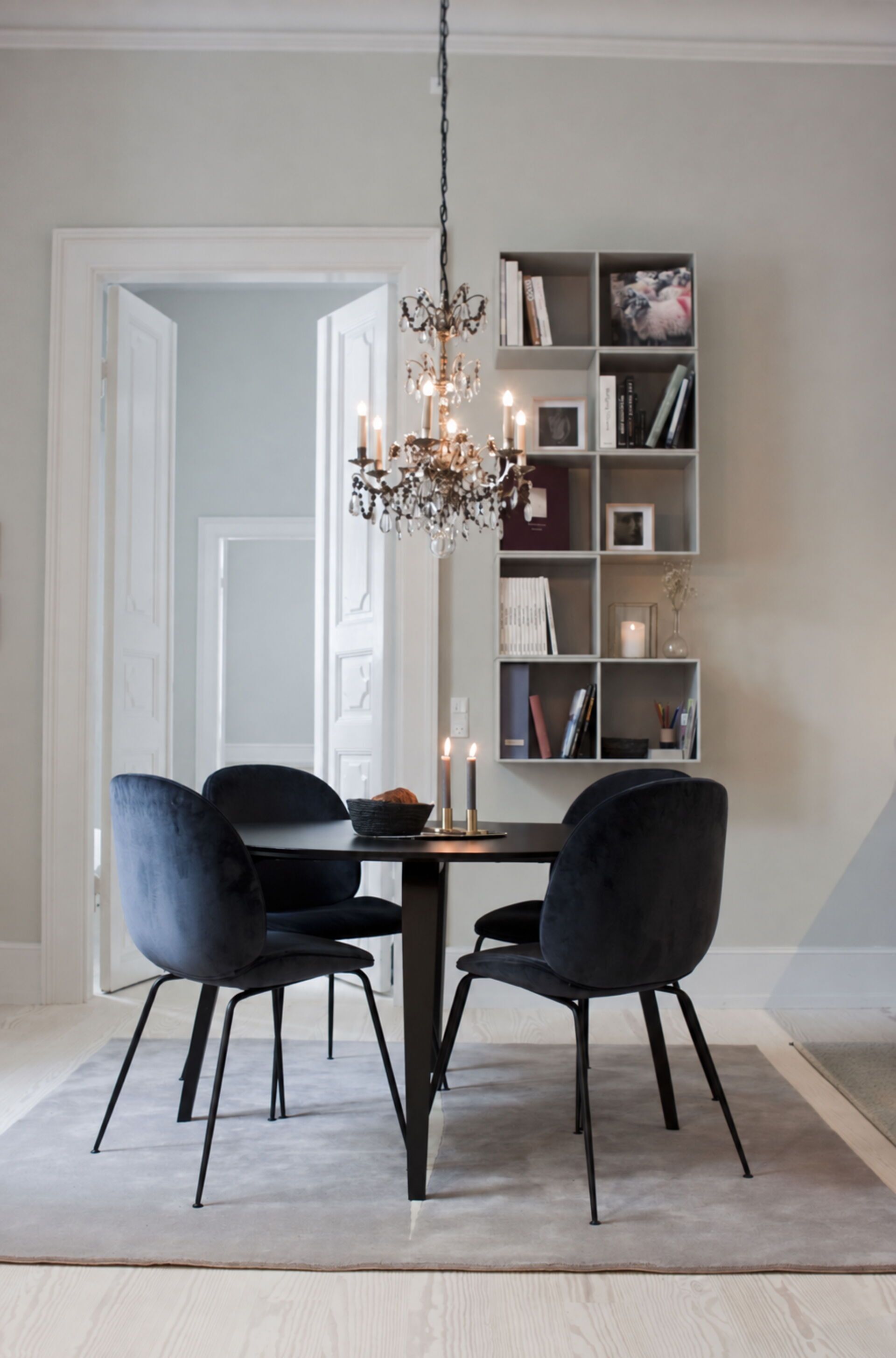 A dining area with a chandelier, two chairs, a table, and a bookshelf.