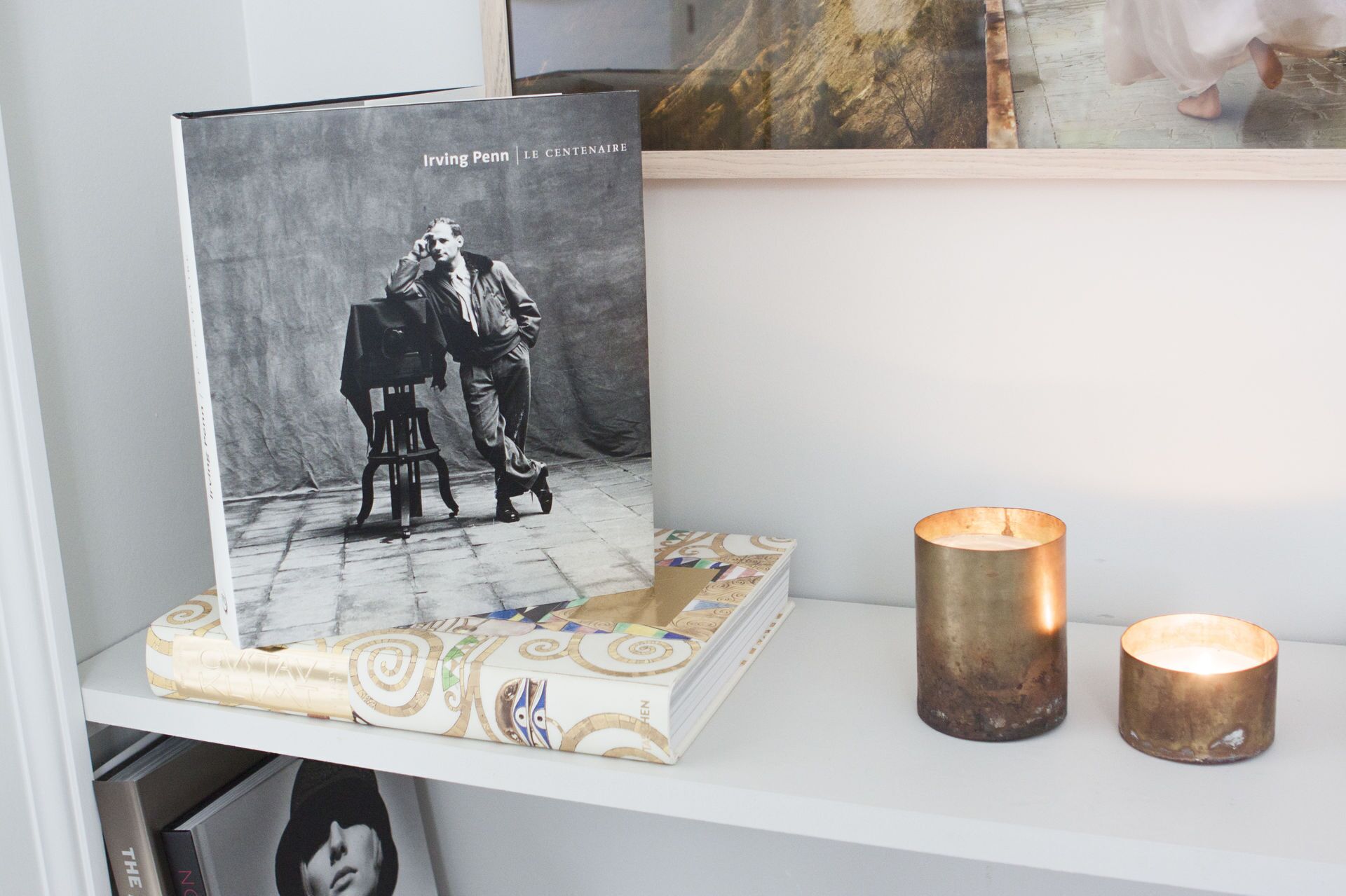 A book titled 'Irving Penn | Le Centenaire' on a shelf, accompanied by two lit candles.
