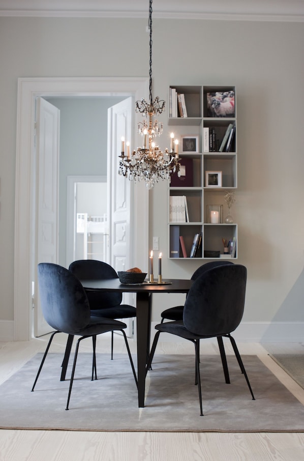 Zona pranzo con un lampadario, due sedie, un tavolo e una libreria con libri e una candela.