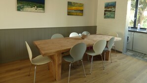 Un comedor con mesa de madera y sillas blancas, una cocina con lavadora, y tres cuadros en la pared.
