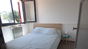Un dormitorio con una cama, una mesita de noche con lámpara y una ventana con persianas.