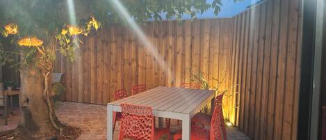 Une terrasse extérieure avec une table en bois et des chaises rouges, entourée d’une clôture en bois et d’un arbre.