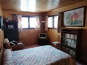Um quarto aconchegante com uma cama, uma estante, uma mesa com um computador, uma cadeira e uma janela com cortinas.